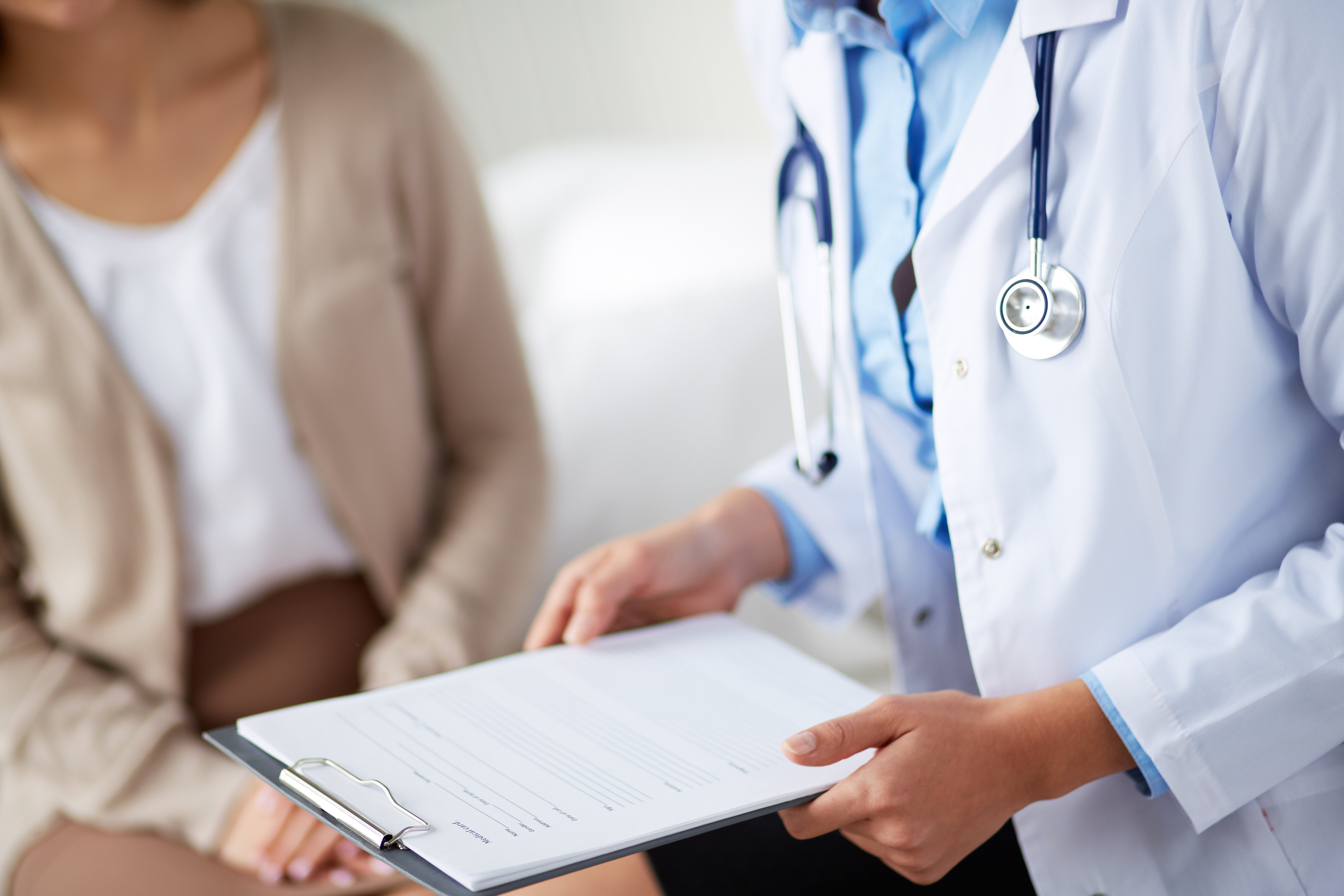 Doctor holding clipboard while speaking to patient.